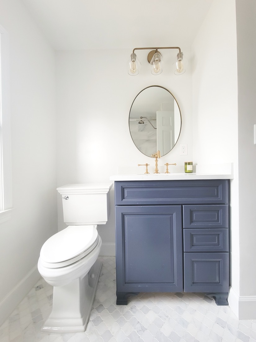 Powder bath with navy vanity, brass fixtures, and marble herringbone floor