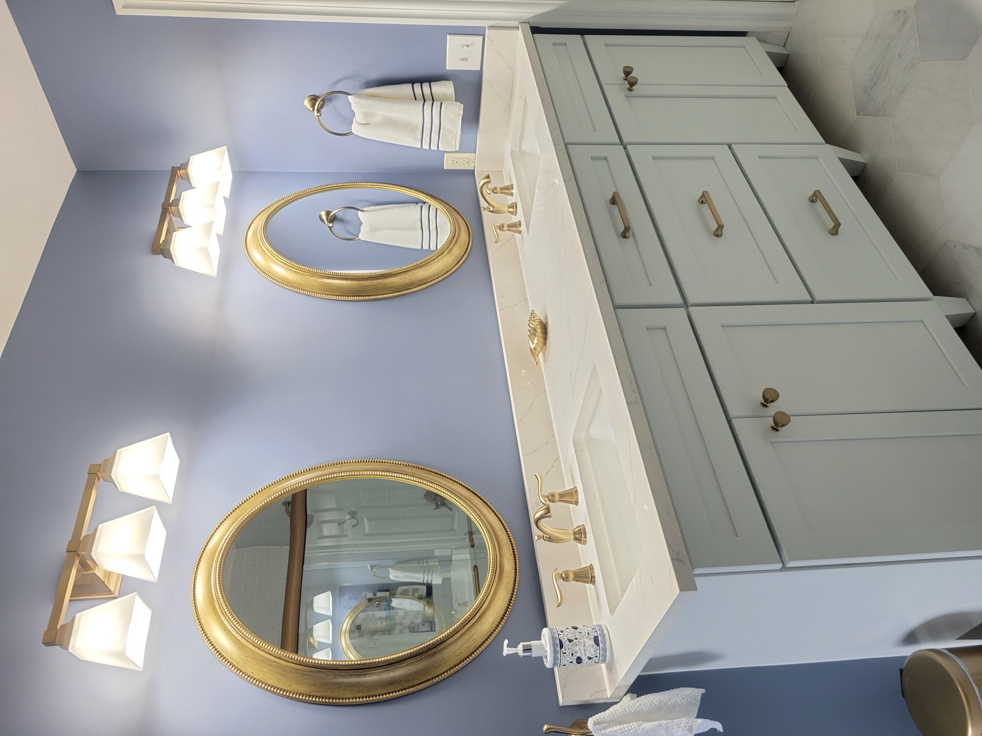 Blue bathroom with gold oval mirrors and light green double vanity