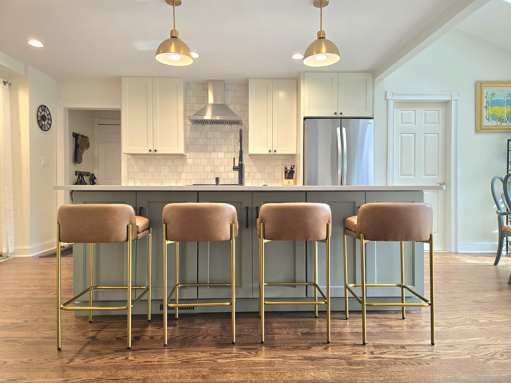 Sage green kitchen island with brass pendants and leather stools